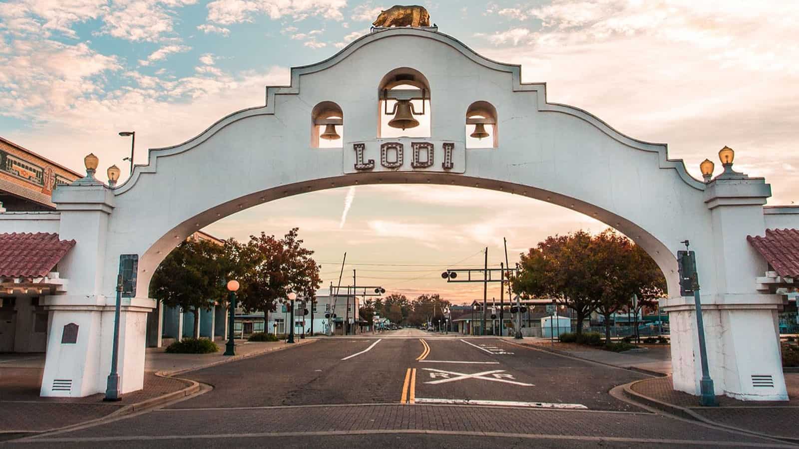 A white archway with bells in the over the middle of a street in the city of Lodi, California with three bells and large golden bear statue