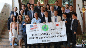 A group of people posing for a picture holding a banner that reads Oakland-Fukuoka Sister City Association established 1962.