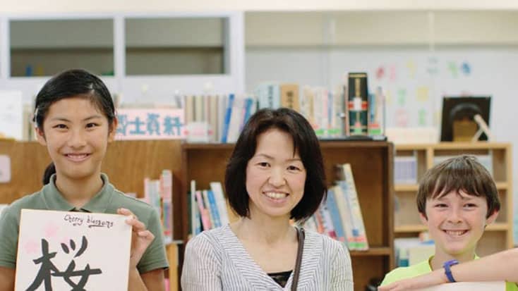 A group of Sunnyvale students visit Iizuka in Japan, holding up signs in a library.