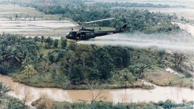 A helicopter spraying Agent Orange during the Vietnam War with jungle and river in the background