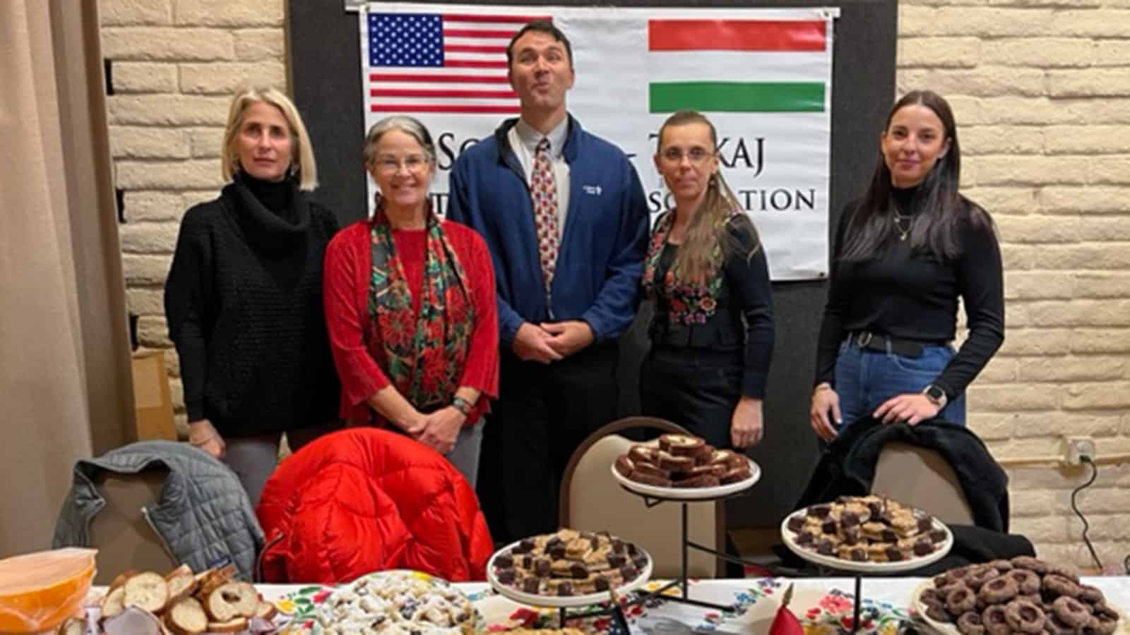 A group of people standing in front of a table with desserts at the Sonoma-Tokaj Committee table during 2022 holiday party.